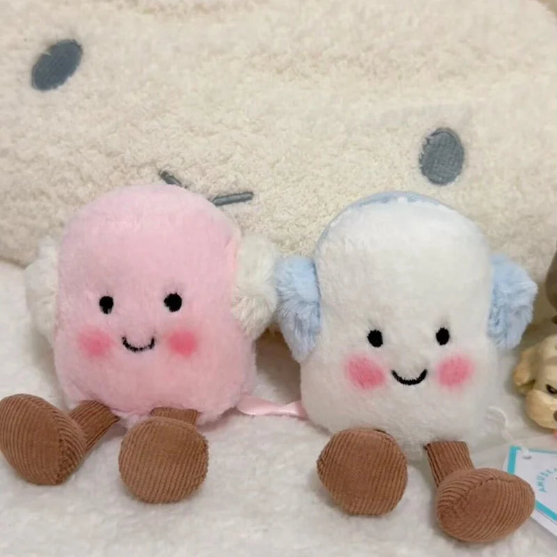 A set of two fluffy marshmallow plush toys, one pink and one white, resting on a white surface.