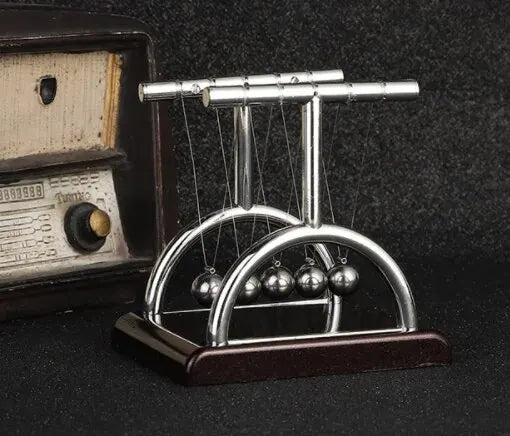 A silver Newton's cradle with balance balls on a dark wooden base.