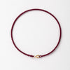 A handmade red string bracelet with a gold plated clasp laid flat against a white background.