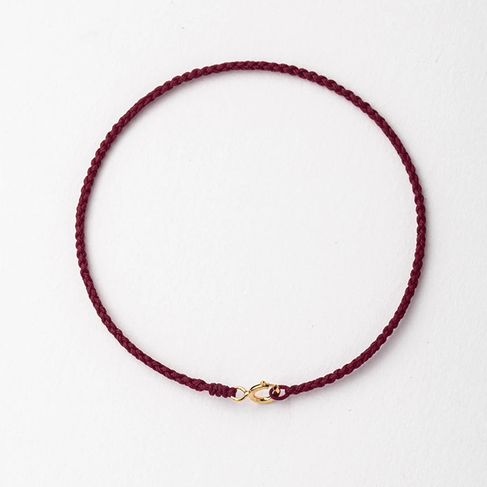 A handmade red string bracelet with a gold plated clasp laid flat against a white background.