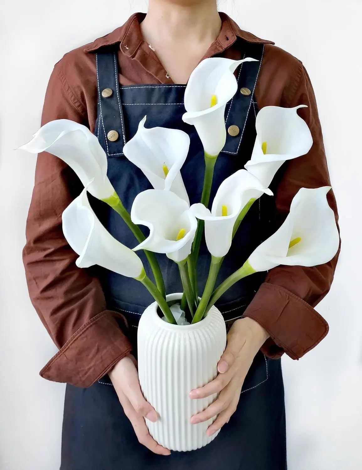A person holds a bouquet of white calla lily artificial flowers in a white vase.