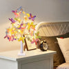 A decorative light display featuring 24 LED butterfly birch tree lights with a warm glow on a bedside table.