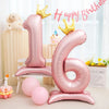 Pink foil number balloon shaped like the number 1 and 6 with gold crowns on a white stand