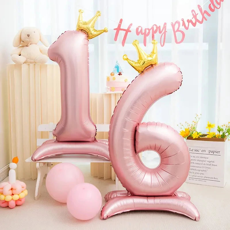 Pink foil number balloon shaped like the number 1 and 6 with gold crowns on a white stand