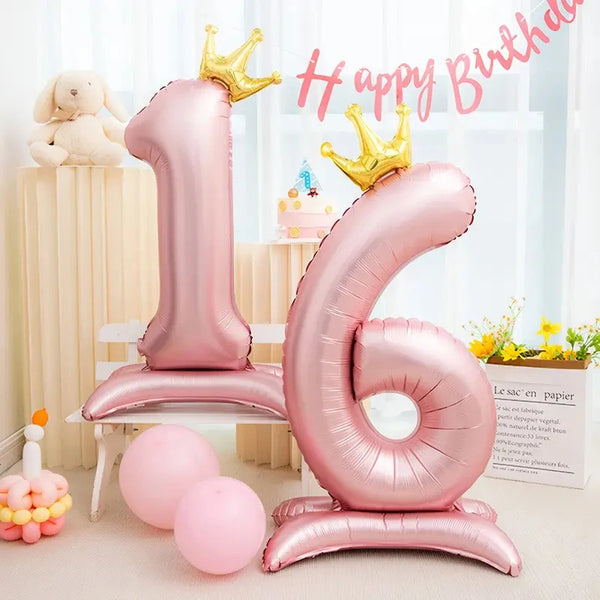 Pink foil number balloon shaped like the number 1 and 6 with gold crowns on a white stand