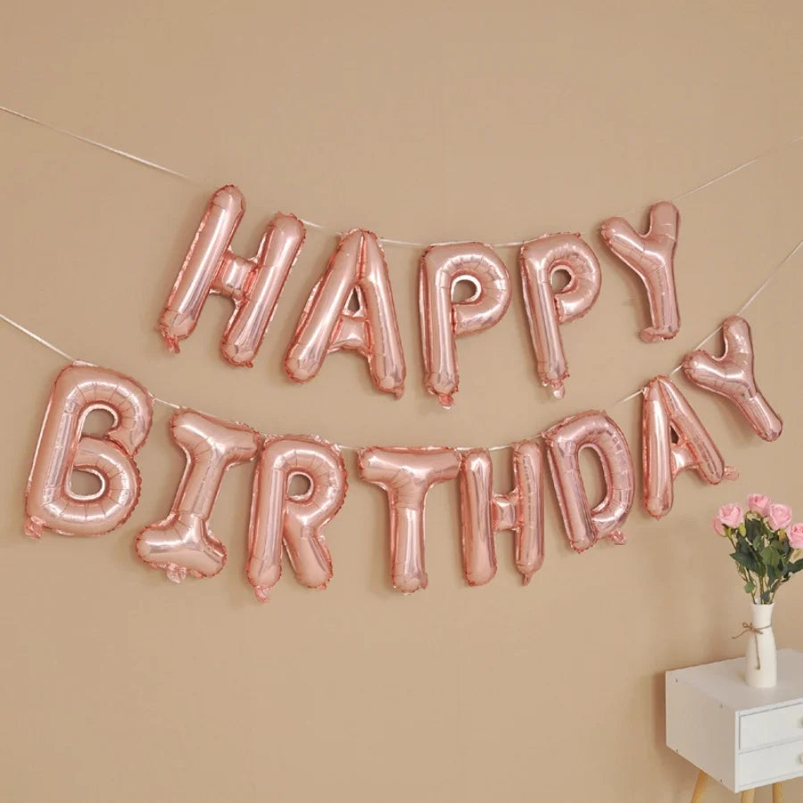 A banner of pink foil letter balloons spelling out Happy Birthday decorating a beige wall.