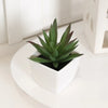A small green artificial succulent plant in a white pot sitting on a white surface.