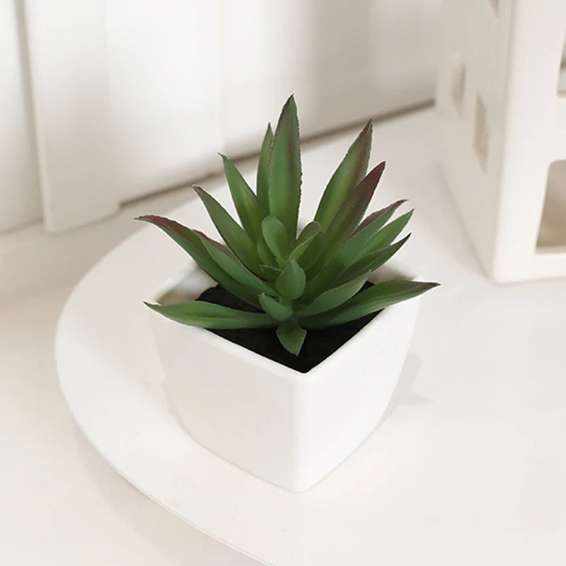 A small green artificial succulent plant in a white pot sitting on a white surface.