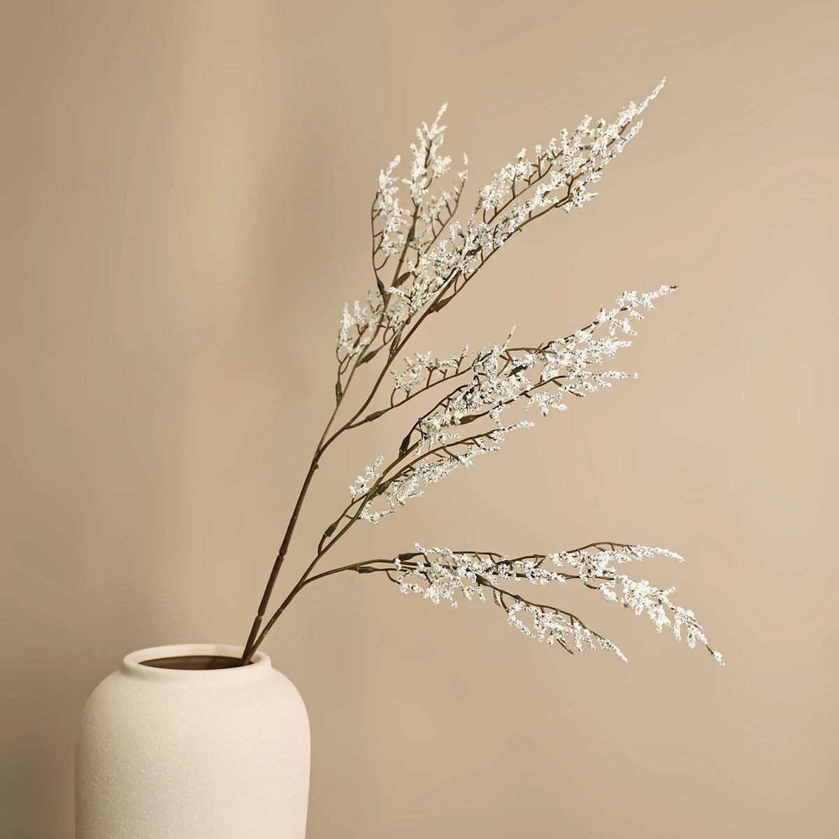 A sprig of artificial silk lover grass with white blossoms displayed in a light colored vase.