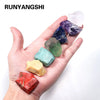 A hand holds a set of natural crystal healing stones displaying various colors including purple, blue, green, and red.
