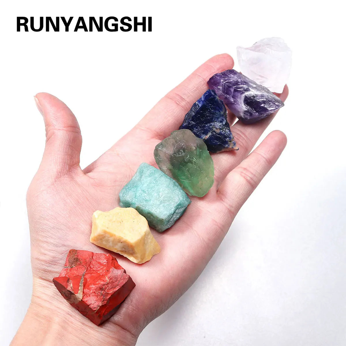 A hand holds a set of natural crystal healing stones displaying various colors including purple, blue, green, and red.
