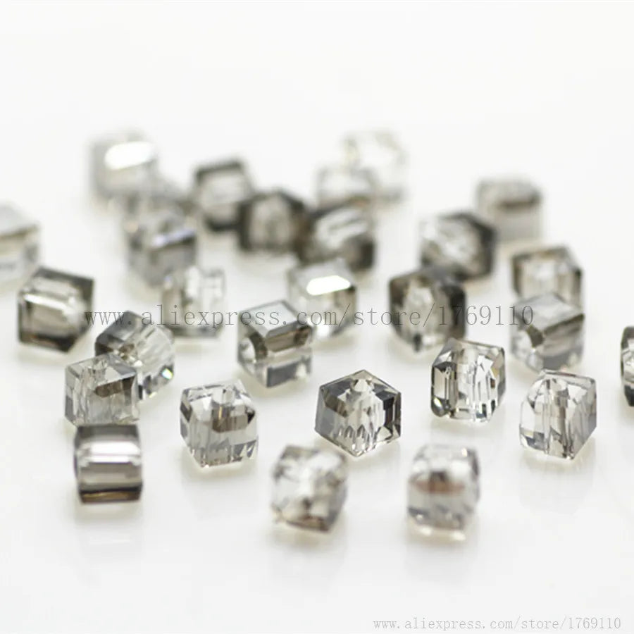 A collection of clear, square cut glass crystal beads for jewelry making scattered on a white surface.