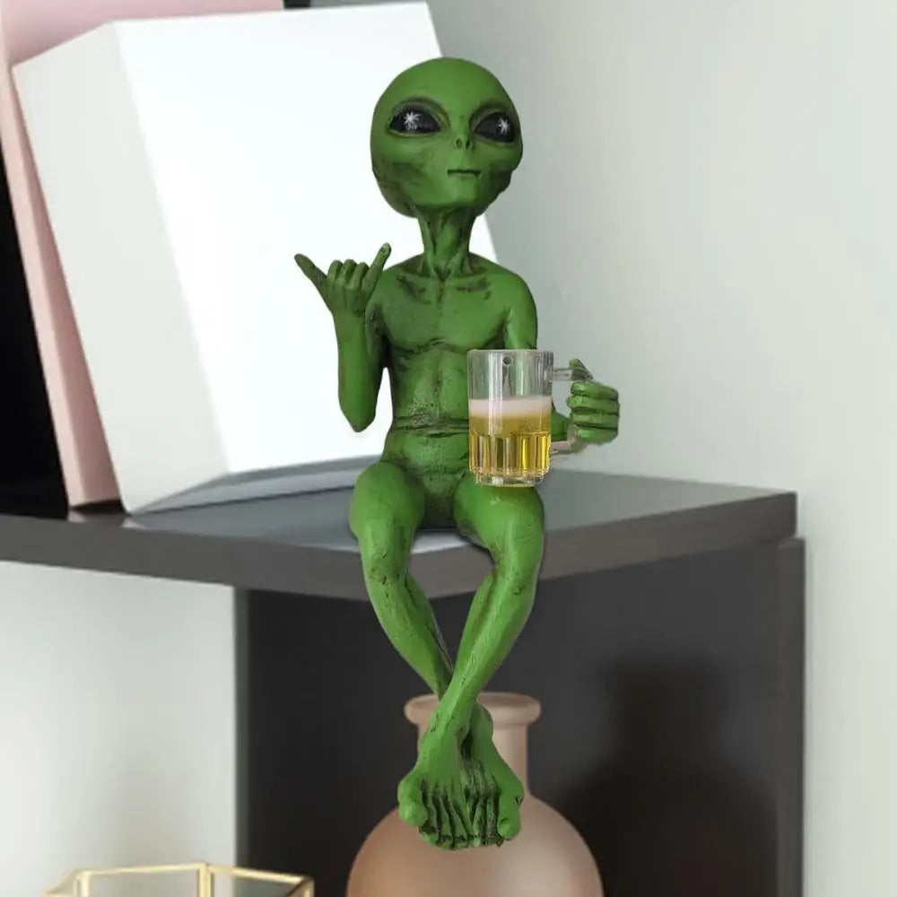 A green alien statue with arms and legs holding a beer mug, displayed on a dark surface.