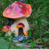 A resin mushroom house garden statue featuring a large, reddish-orange toadstool with a small house structure beneath it.