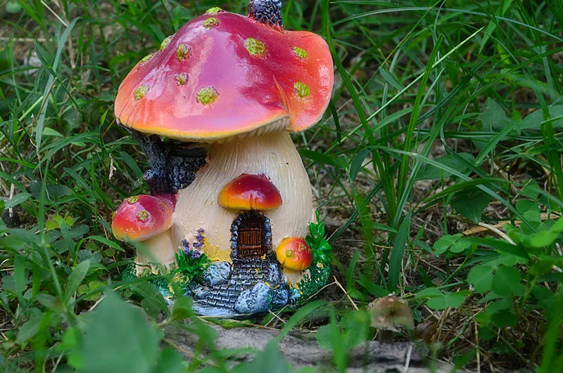 A resin mushroom house garden statue featuring a large, reddish-orange toadstool with a small house structure beneath it.