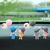 A set of cute couple figurines with balloons displayed on a car dashboard.