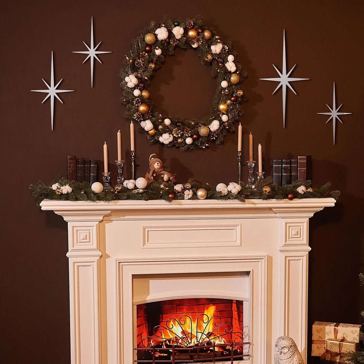 A mantelpiece decorated with a wreath, candles, and metal star wall art on a dark brown wall.