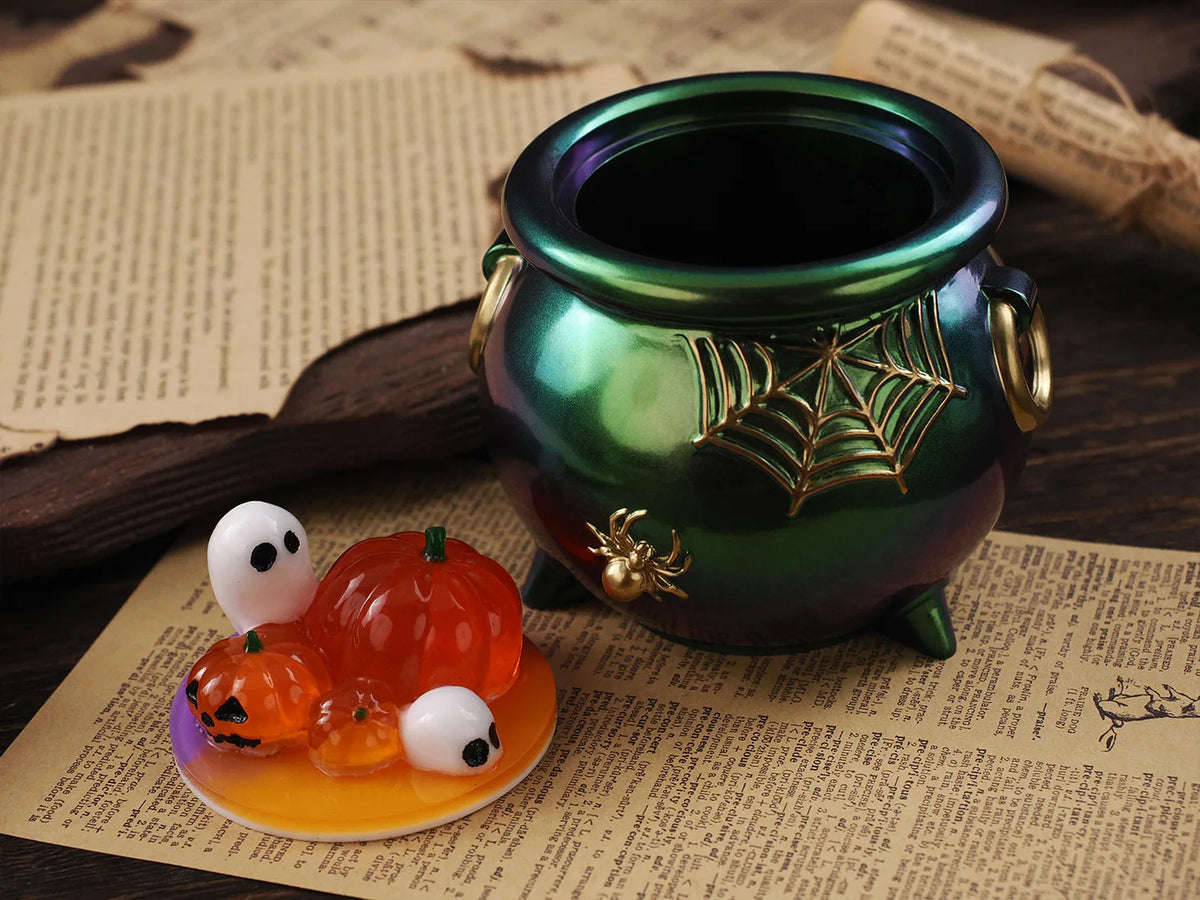 A green ceramic jar with a gold spider design sits on parchment paper next to silicone Halloween pumpkin molds.