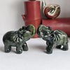 A pair of carved jade elephant statues resting on a white surface next to a red vase and silver object.