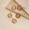 A set of five gold-toned double-sided St. Benedict medals displayed on a light stone surface.