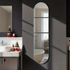 A vertical oval mirror reflects a bathroom interior, showing a sink and shower area on a dark gray wall.