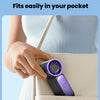A hand places a purple and black portable handheld fan into a pocket of a light-colored bag.