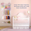 A white crib with a pink bedding set and a wall-mounted storage rack for baby headbands.