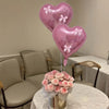 Two pink heart-shaped foil balloons with white ribbon bows displayed on a table.