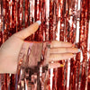 A hand holds metallic pink tinsel foil fringe curtain backdrop for parties.