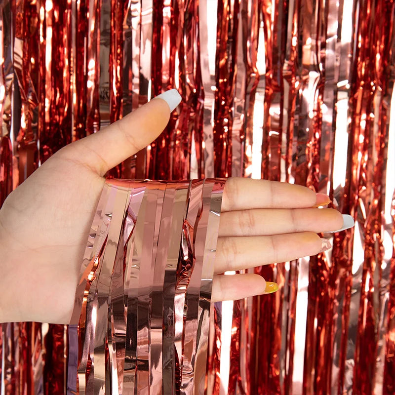 A hand holds metallic pink tinsel foil fringe curtain backdrop for parties.