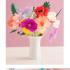 Ein Strauß bunter Krepppapierblumen in Rosa-, Orange-, Violett- und Weißtönen in einer weißen Vase.