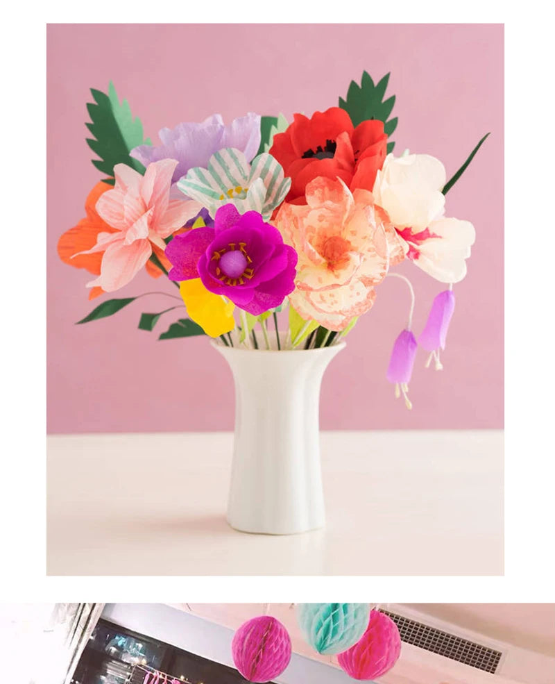 Ein Strauß bunter Krepppapierblumen in Rosa-, Orange-, Violett- und Weißtönen in einer weißen Vase.