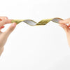 Hands are demonstrating a gold-colored self-adhesive PVC edge guard strip for furniture corners.