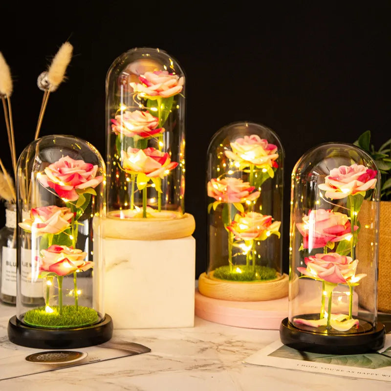 LED Galaxy rose artificial flower displayed in glass domes on a white marble surface.