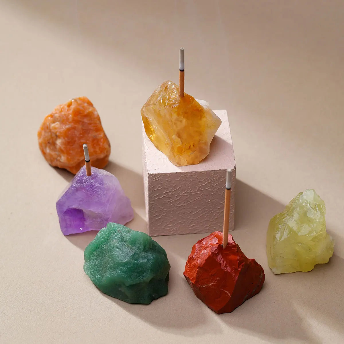 A collection of raw crystal specimens including purple amethyst, yellow quartz, green jade, and red tourmaline mounted on sti