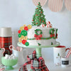A tiered white cake decorated with green and red accents, surrounded by various festive food items.