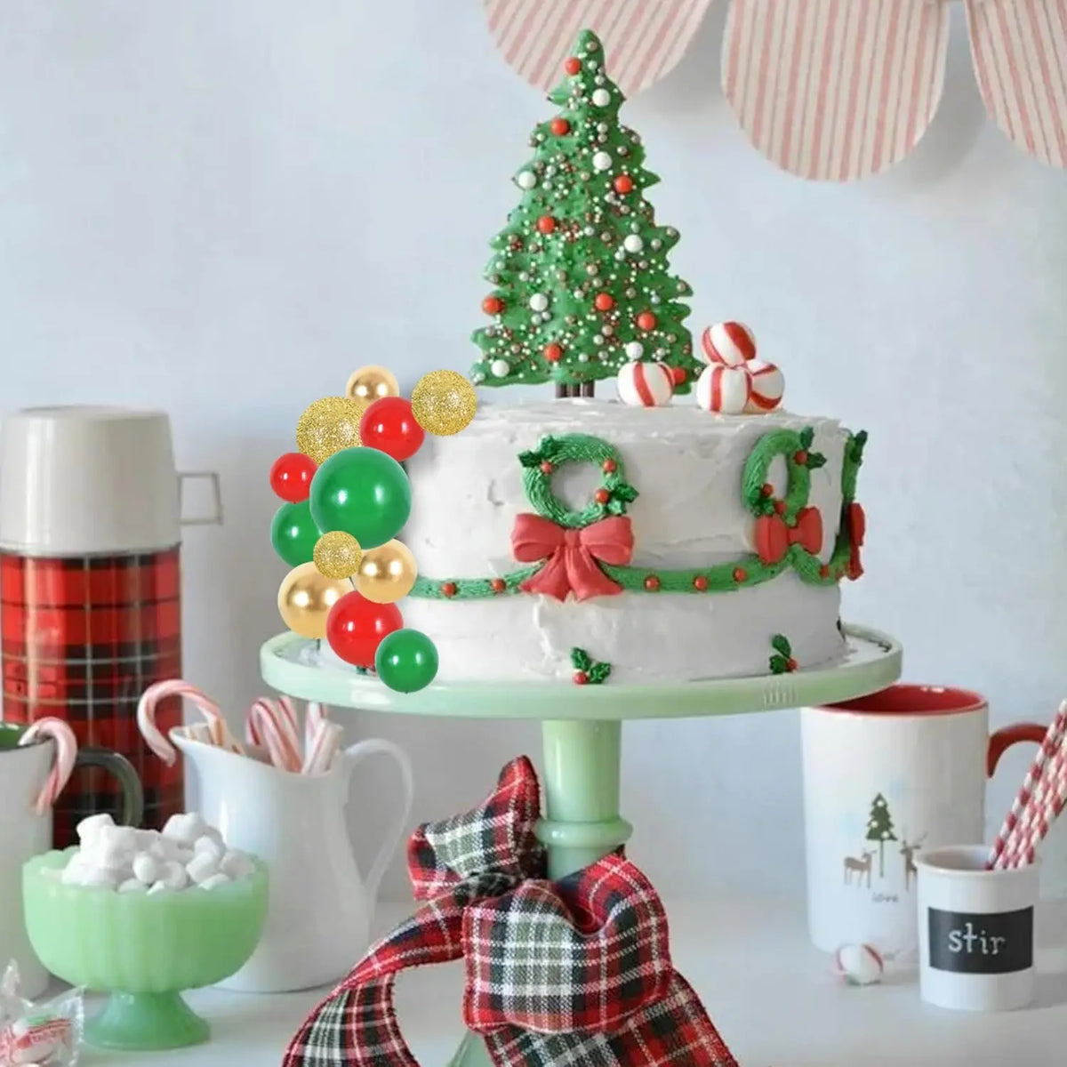 A tiered white cake decorated with green and red accents, surrounded by various festive food items.