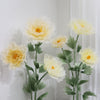 A large artificial silk yellow poppy flower displayed on a green stand against a white wall.
