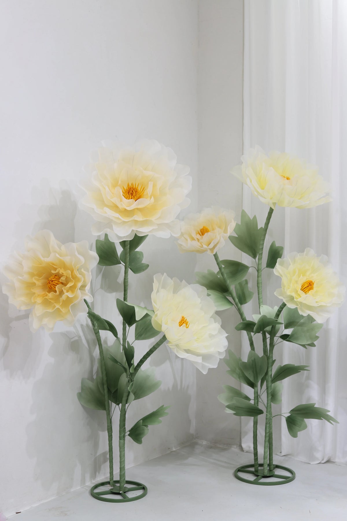 A large artificial silk yellow poppy flower displayed on a green stand against a white wall.