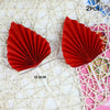 Two red palm leaf cake toppers with pleated design shown on a white woven background.