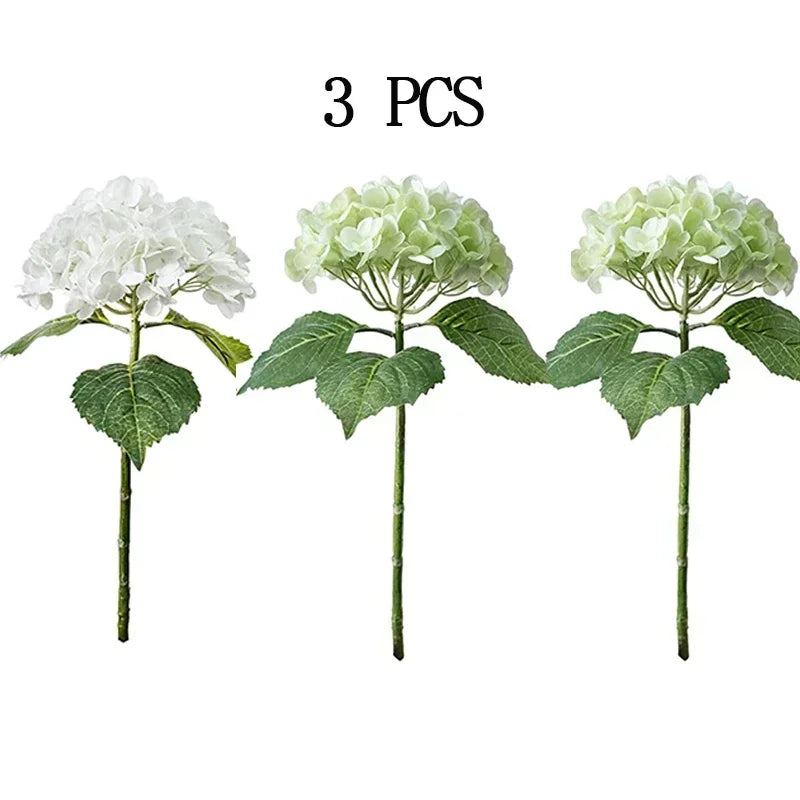 Three stems of artificial white hydrangea flowers with green leaves.