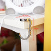 A silver foldable handbag hook is shown attached to a wooden table leg, with measurements indicating its size.