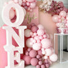 A large pink balloon letter display spelling ONE and AYLA with clusters of pastel pink balloons in a soft pink setting