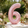 A large pink foil number balloon shaped like the number six with bows, displayed outdoors on a white table.