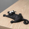 Schwarze magnetische Katzenfigur mit weißen Augen und Schnurrhaaren auf einer Holzoberfläche.