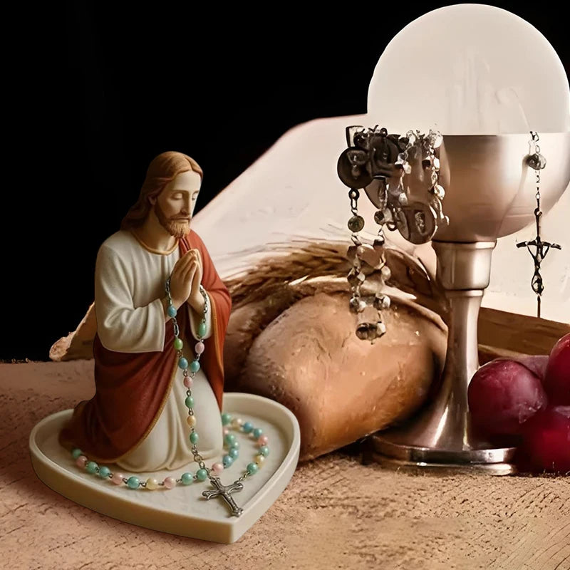 A statue of Jesus with a rosary holder and pearls displayed on a light-colored tray.