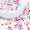 A white container filled with colorful frosted glass rice beads scattered around it.