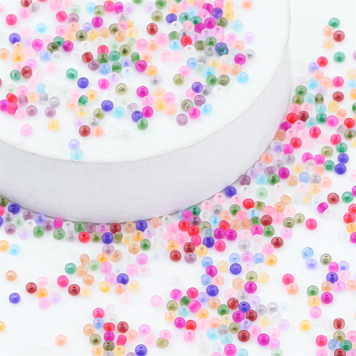 A white container filled with colorful frosted glass rice beads scattered around it.