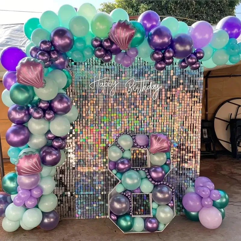 A colorful balloon arch and square wall backdrop decorated with iridescent and metallic balloons for a birthday party.