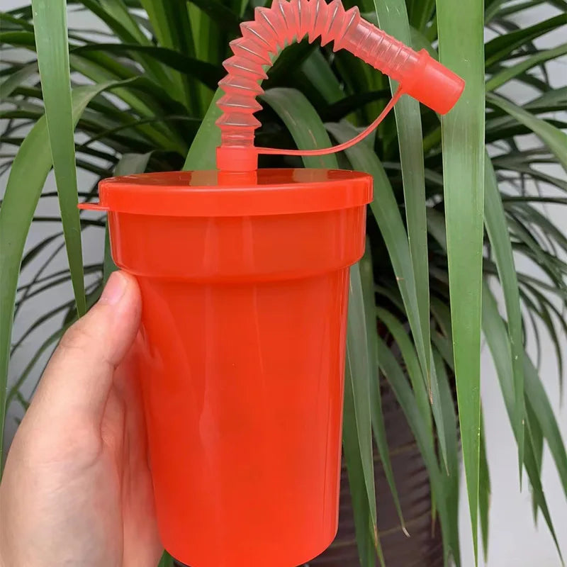 An orange reusable sipper cup with a pink straw is being held against a background of green foliage.
